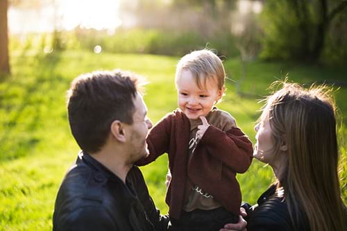 Parents smiling with their toddler outdoors.