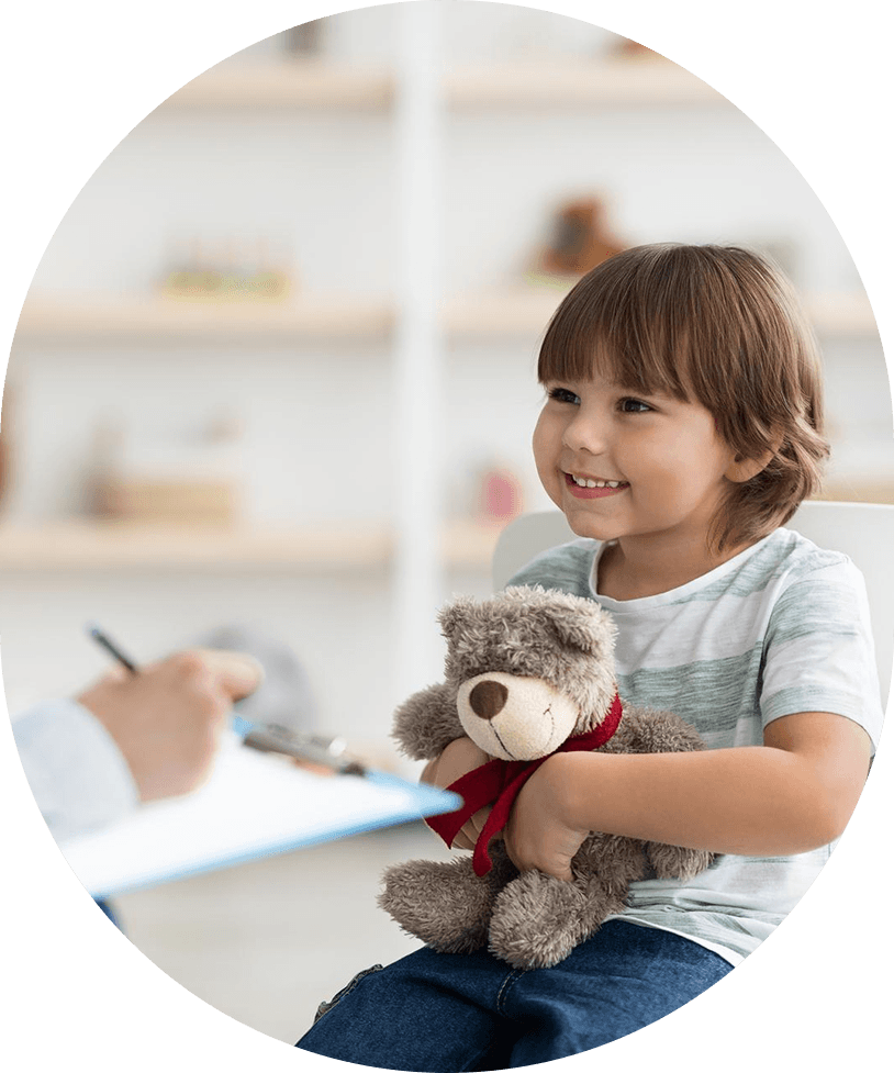 Child smiling and holding a teddy bear during an ABA therapy session.