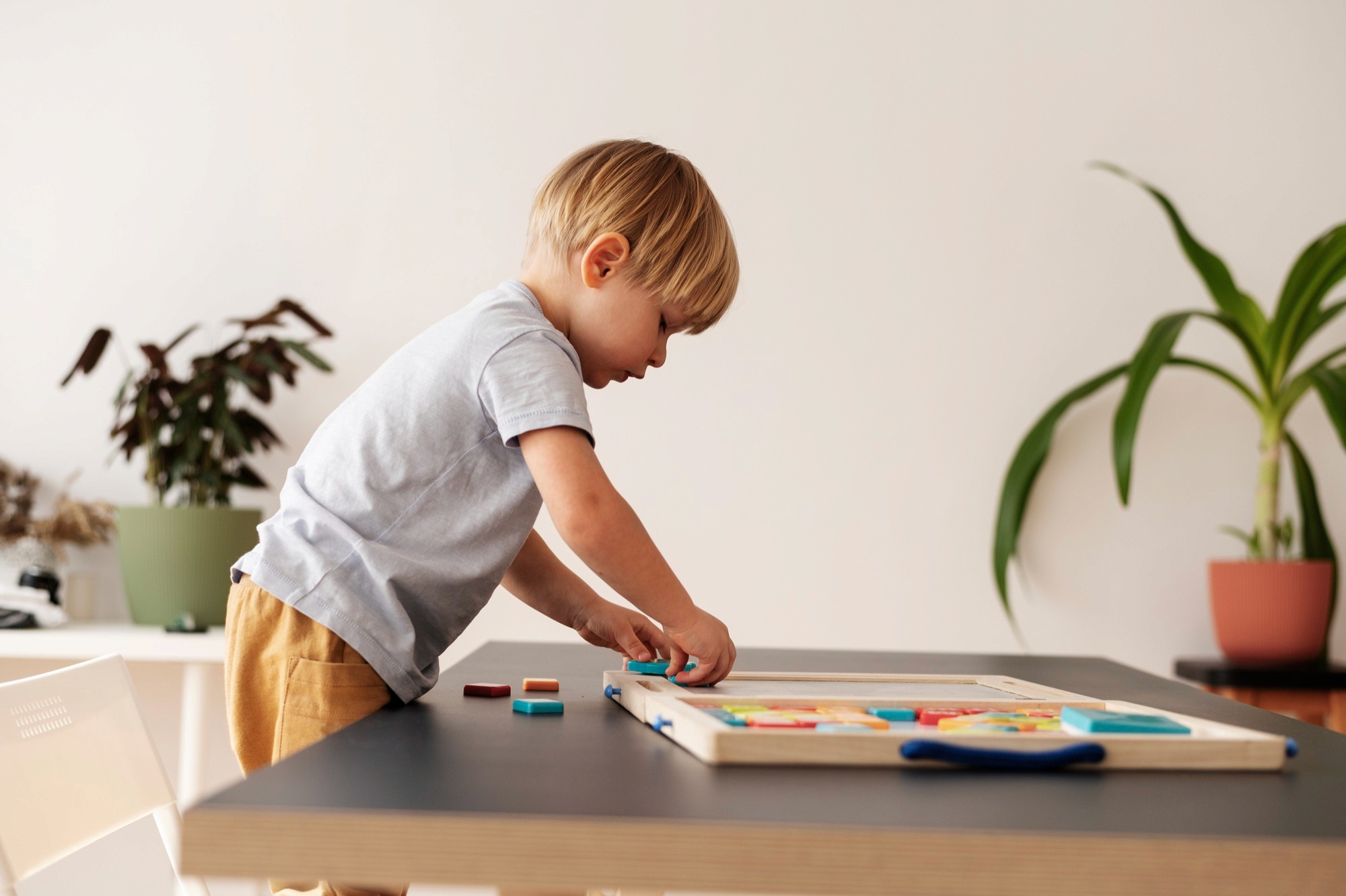 Young boy placing a wooden puzzle piece on a table.